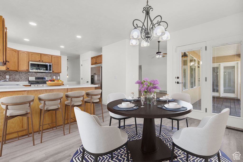 Dining space featuring ceiling fan with notable chandelier, light hardwood / wood-style floors, and sink