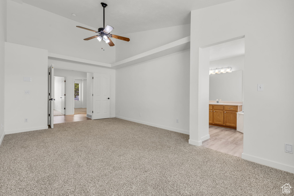 Unfurnished bedroom featuring ensuite bathroom, sink, light colored carpet, high vaulted ceiling, and ceiling fan