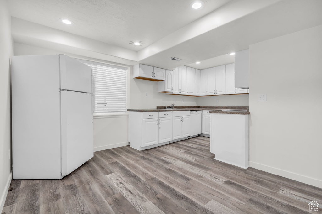 Kitchen with white cabinetry, sink, white appliances, and light wood-type flooring