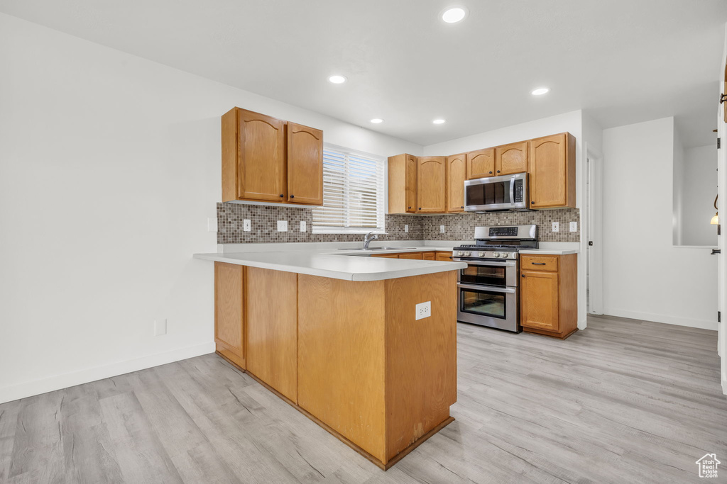 Kitchen featuring stainless steel appliances, decorative backsplash, sink, light hardwood / wood-style floors, and kitchen peninsula