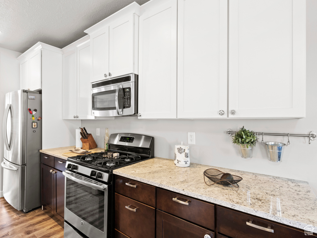 Kitchen with appliances with stainless steel finishes, light stone counters, white cabinets, and light hardwood / wood-style floors