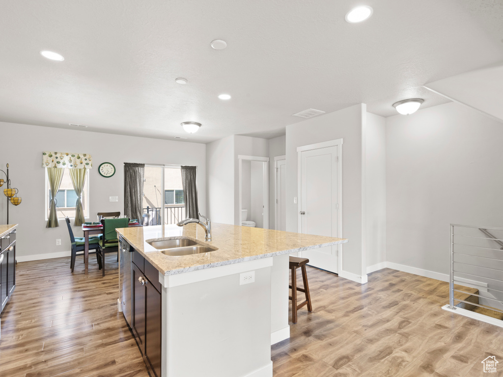 Kitchen featuring light hardwood / wood-style flooring, light stone counters, sink, a kitchen breakfast bar, and a center island with sink