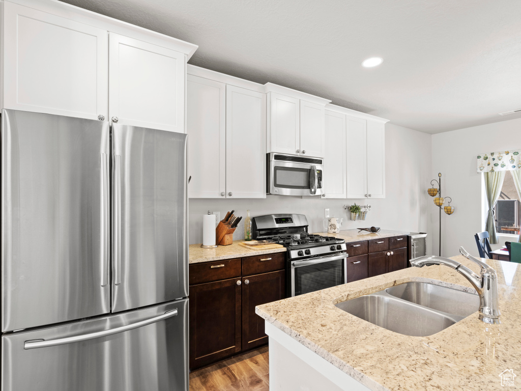 Kitchen with light hardwood / wood-style floors, appliances with stainless steel finishes, white cabinets, and sink