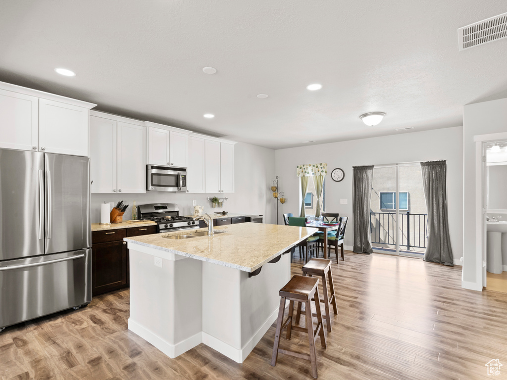 Kitchen with white cabinetry, stainless steel appliances, sink, a center island with sink, and light hardwood / wood-style floors