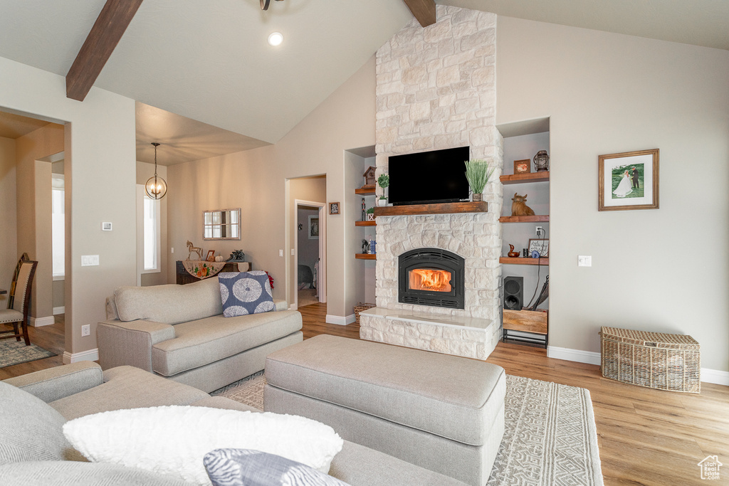 Living room featuring light hardwood / wood-style floors, beamed ceiling, built in shelves, high vaulted ceiling, and a stone fireplace