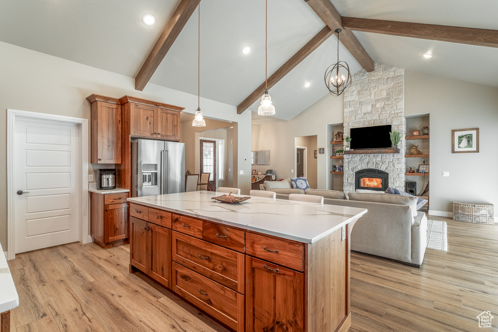 Kitchen featuring light wood-type flooring, hanging light fixtures, a kitchen island, a fireplace, and high end refrigerator