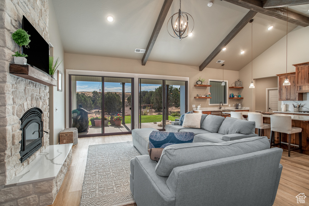 Living room with an inviting chandelier, beamed ceiling, light hardwood / wood-style flooring, and a fireplace