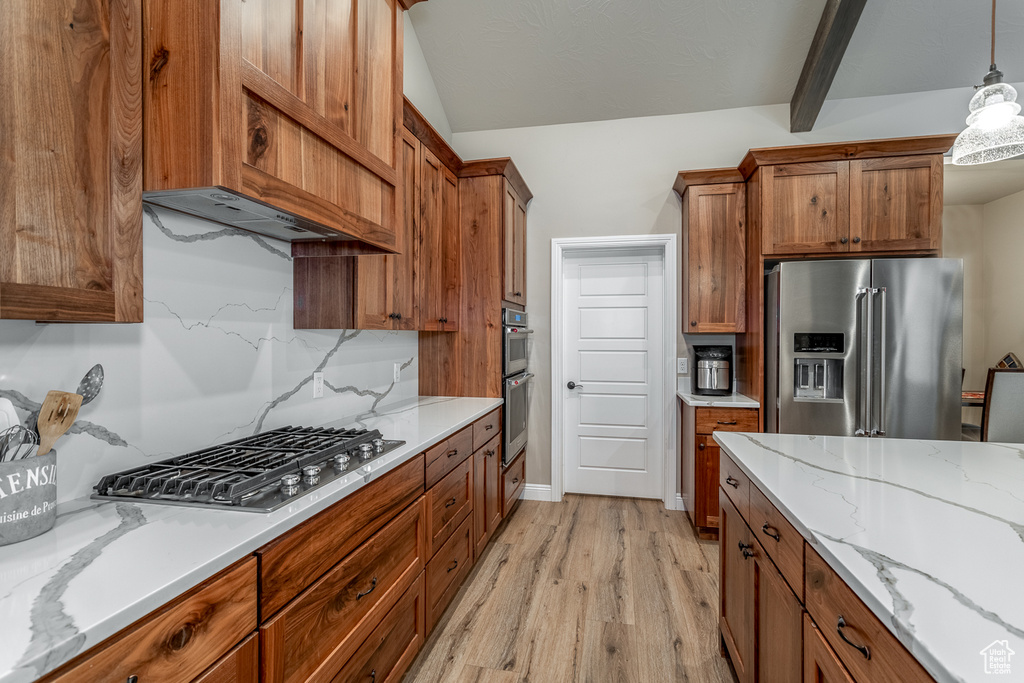 Kitchen with light stone counters, light hardwood / wood-style floors, lofted ceiling, stainless steel appliances, and decorative light fixtures