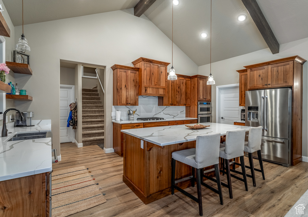 Kitchen featuring beam ceiling, decorative light fixtures, stainless steel appliances, light wood-type flooring, and a kitchen bar