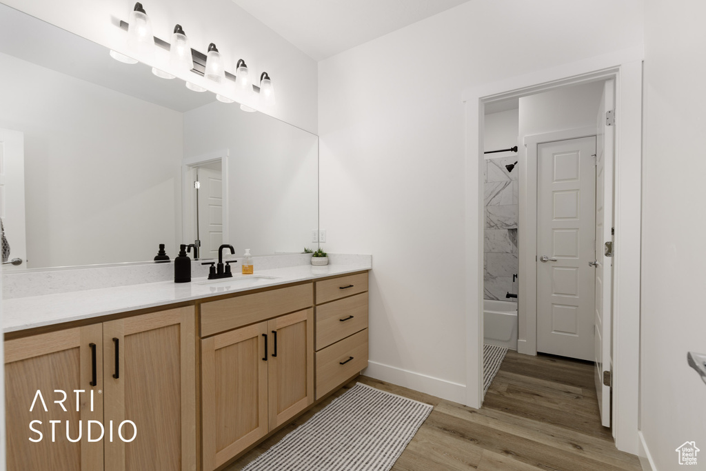 Bathroom with tiled shower / bath combo, vanity, and hardwood / wood-style floors