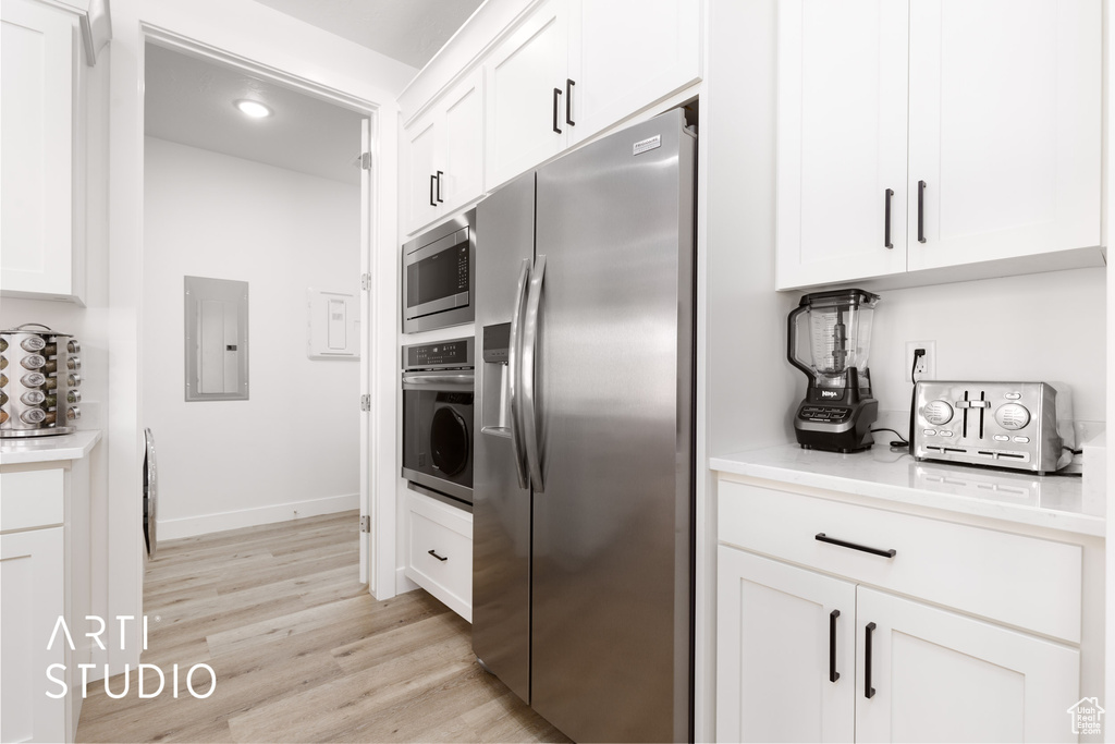 Kitchen with white cabinetry, light wood-type flooring, stainless steel appliances, and electric panel