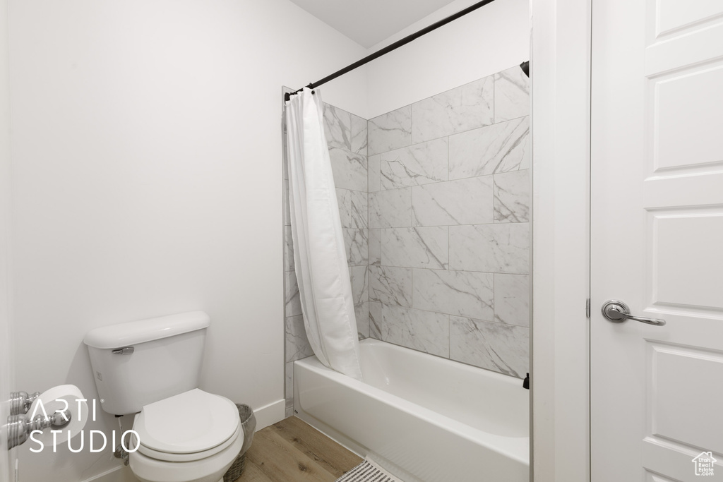 Bathroom with wood-type flooring, shower / bathtub combination with curtain, and toilet