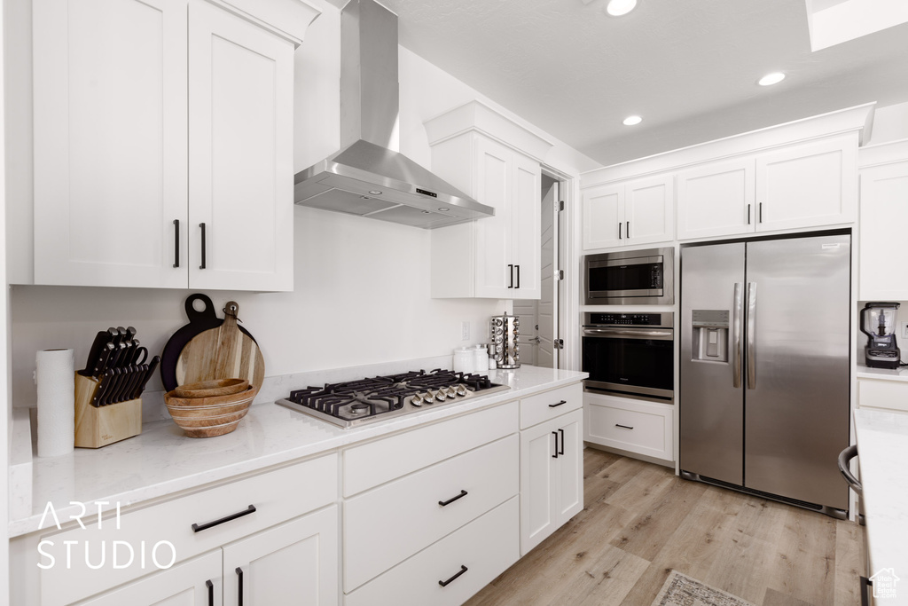 Kitchen with wall chimney range hood, white cabinetry, light wood-type flooring, and stainless steel appliances