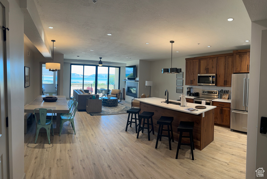 Kitchen featuring light hardwood / wood-style flooring, an island with sink, stainless steel appliances, pendant lighting, and a kitchen bar