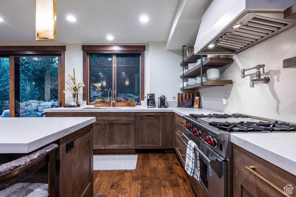 Kitchen featuring designer stove, sink, light stone counters, dark hardwood / wood-style floors, and custom range hood