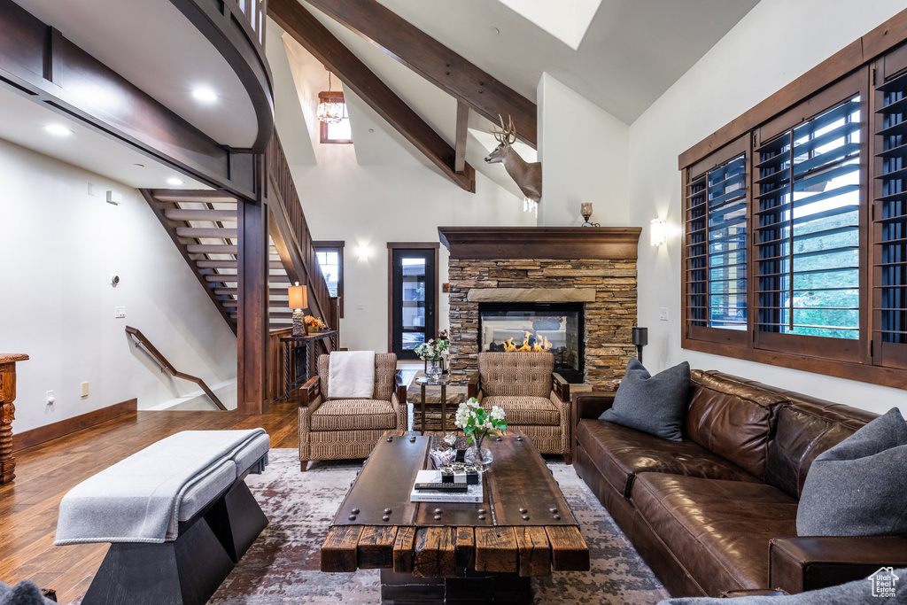 Living room with a stone fireplace, beamed ceiling, dark hardwood / wood-style flooring, and high vaulted ceiling