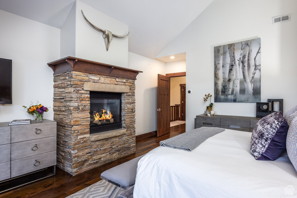 Bedroom featuring a stone fireplace, dark wood-type flooring, and high vaulted ceiling