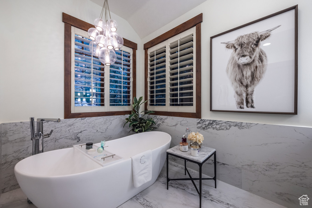 Bathroom featuring tile patterned floors, tile walls, a chandelier, a tub, and vaulted ceiling