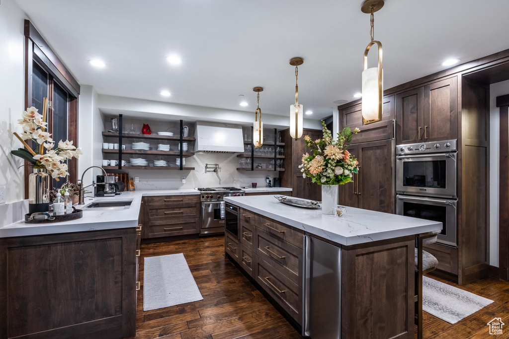 Kitchen with custom exhaust hood, pendant lighting, sink, high end appliances, and dark wood-type flooring