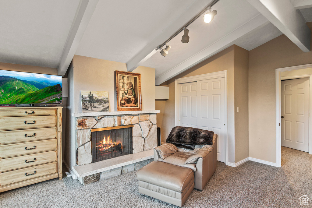 Sitting room featuring vaulted ceiling with beams, a stone fireplace, rail lighting, and carpet