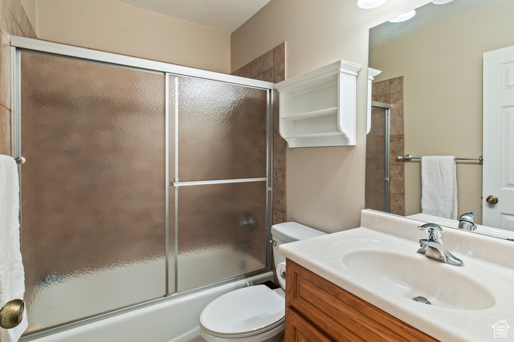 Full bathroom with vanity, shower / bath combination with glass door, and toilet