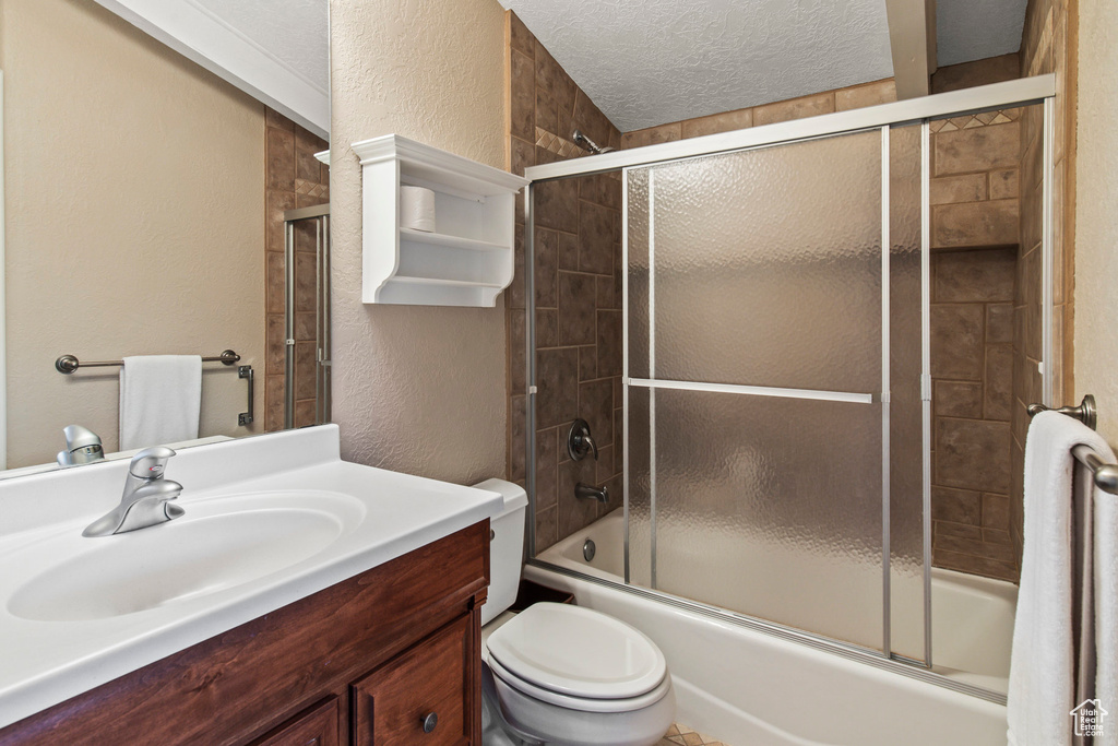 Full bathroom featuring vanity, a textured ceiling, bath / shower combo with glass door, and toilet