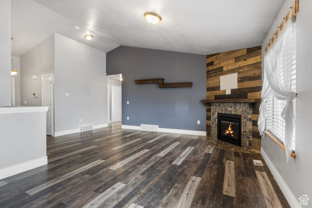 Unfurnished living room featuring wood walls, vaulted ceiling, and dark wood-type flooring