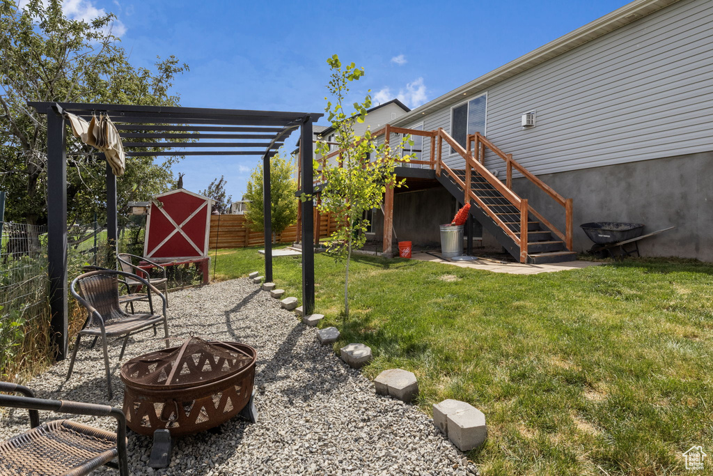 View of yard with an outdoor fire pit, a storage unit, a deck, and a pergola