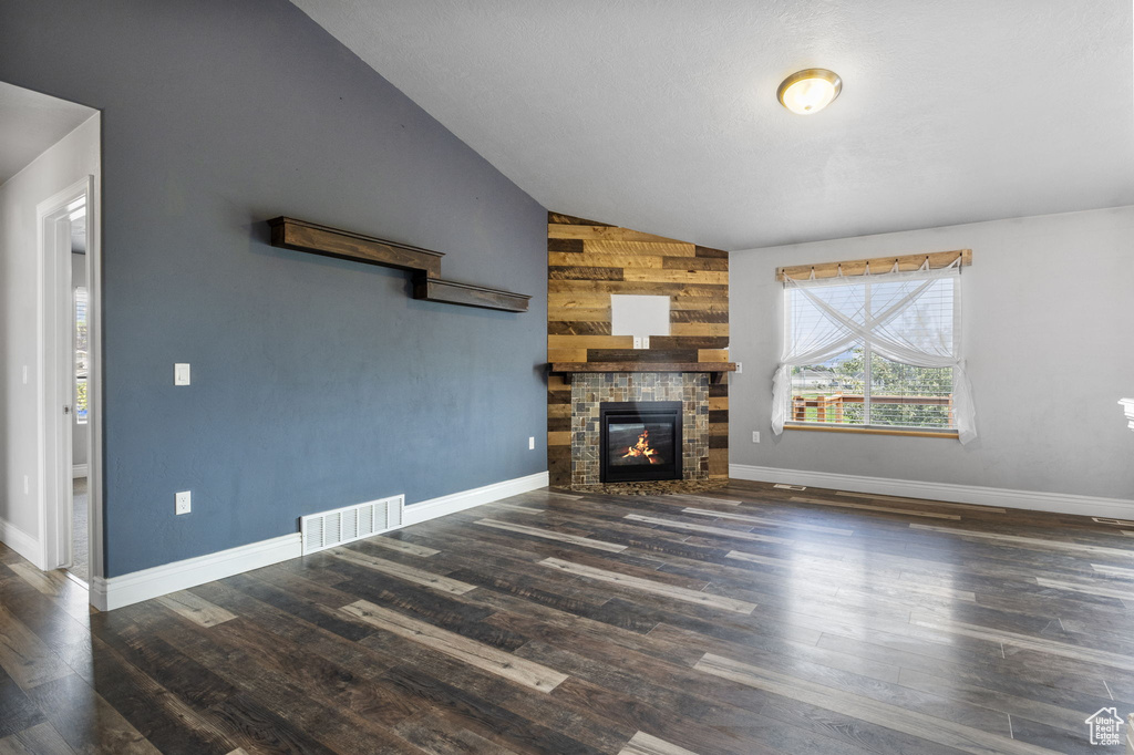 Unfurnished living room featuring wood walls, a fireplace, lofted ceiling, and dark wood-type flooring