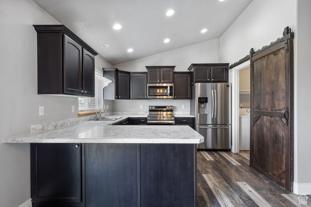 Kitchen featuring appliances with stainless steel finishes, a barn door, dark brown cabinetry, lofted ceiling, and dark hardwood / wood-style flooring