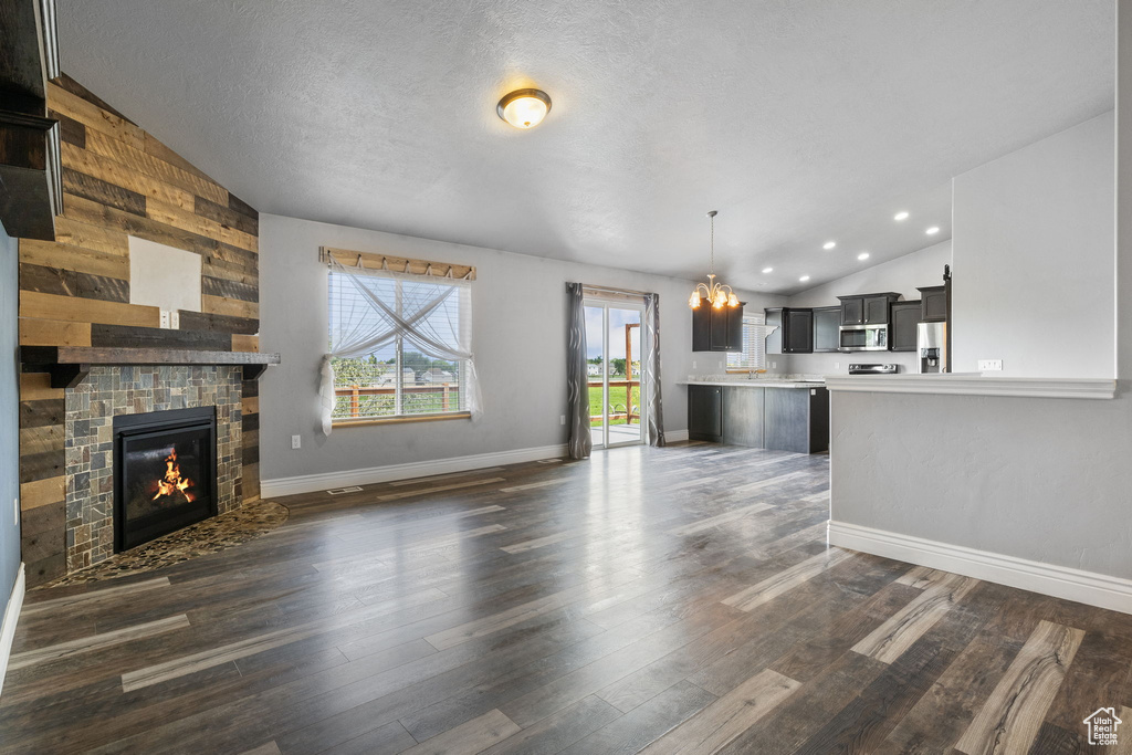 Unfurnished living room featuring an inviting chandelier, a textured ceiling, lofted ceiling, wood walls, and dark wood-type flooring