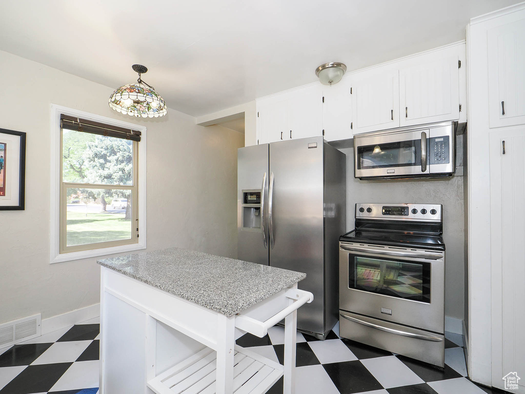 Kitchen featuring white cabinetry, dark tile patterned floors, pendant lighting, and stainless steel appliances