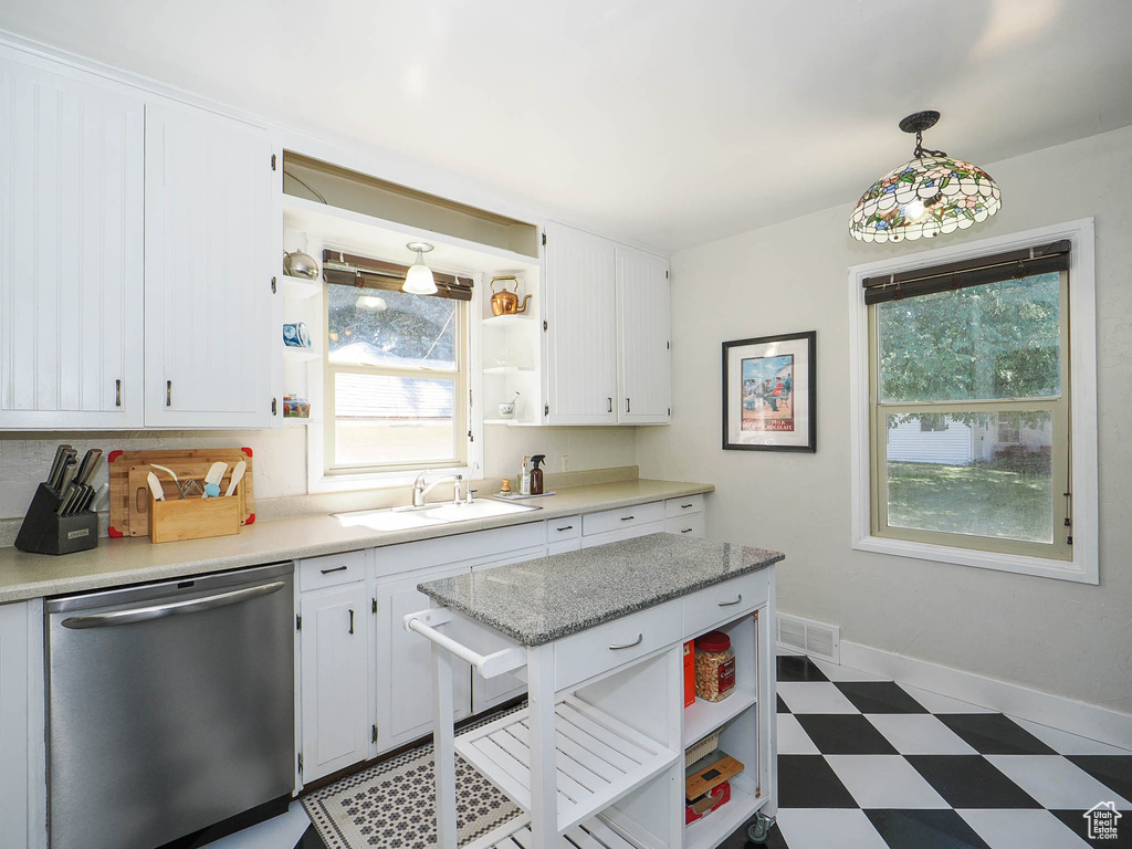 Kitchen with stainless steel dishwasher, decorative light fixtures, white cabinetry, sink, and dark tile patterned flooring