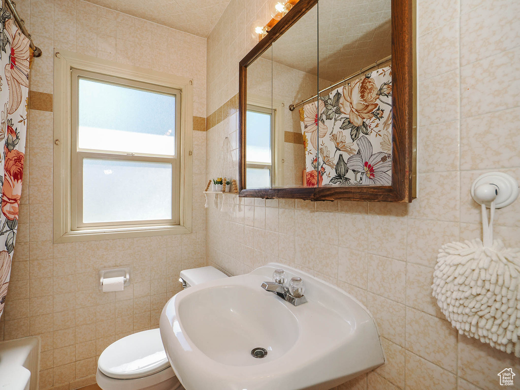 Bathroom featuring sink, tile walls, and toilet