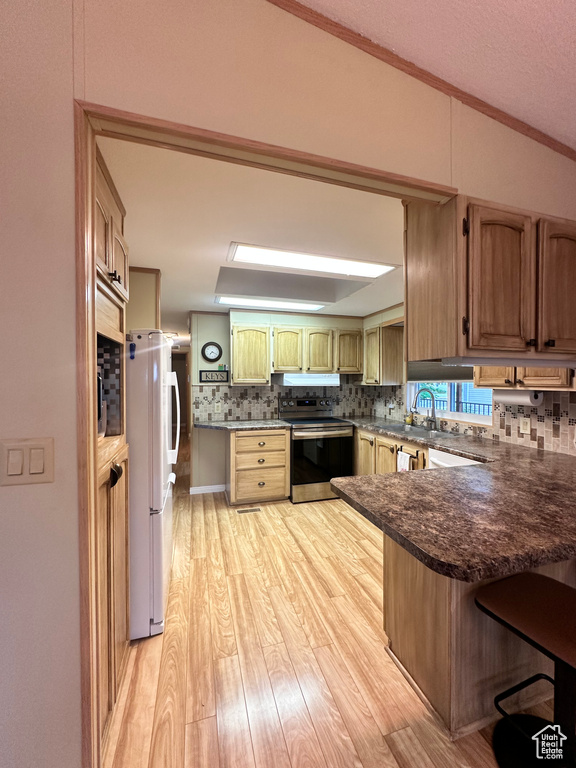 Kitchen featuring white refrigerator, decorative backsplash, stainless steel range with electric stovetop, light hardwood / wood-style flooring, and kitchen peninsula