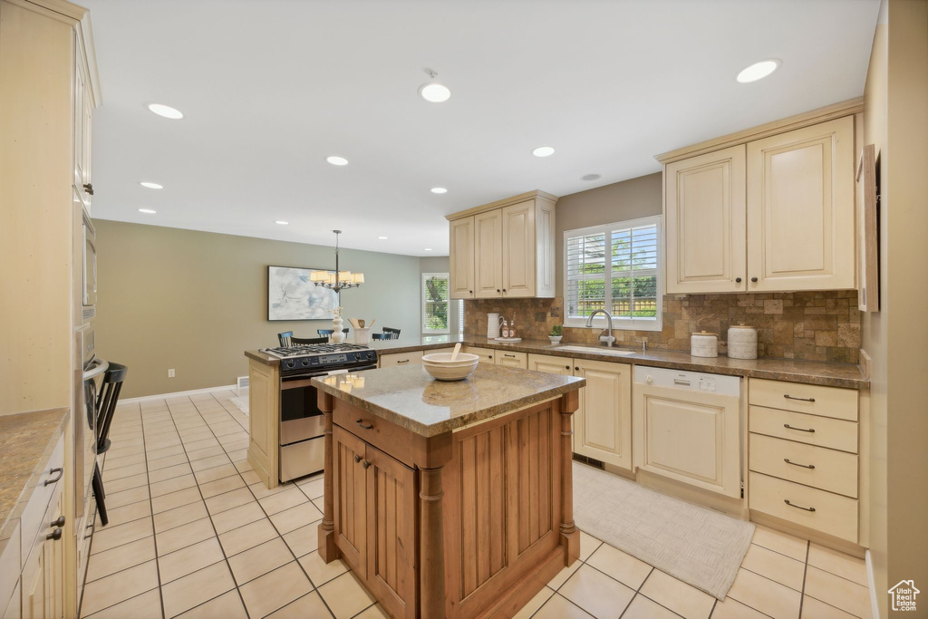 Kitchen with gas range oven, sink, pendant lighting, light tile patterned floors, and decorative backsplash