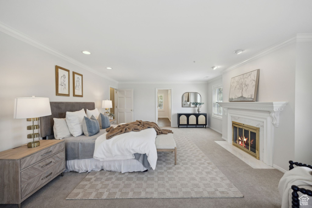 Bedroom with ornamental molding, a premium fireplace, and light colored carpet