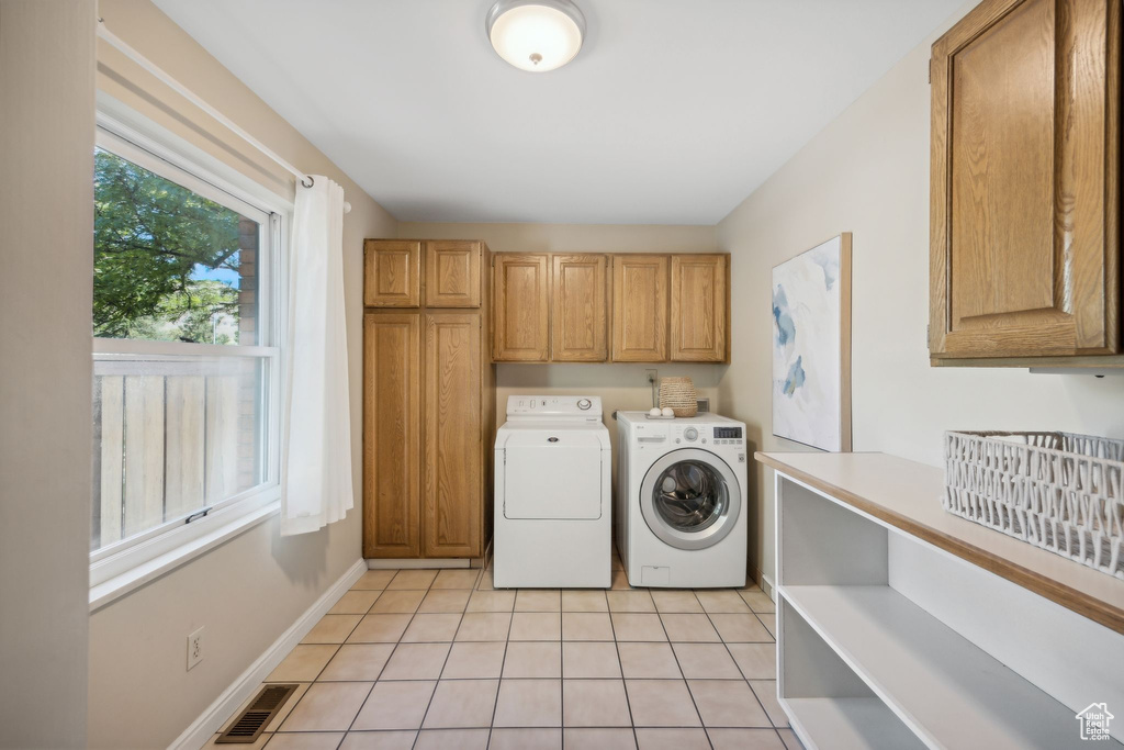 Laundry area featuring cabinets, light tile patterned floors, and washing machine and clothes dryer