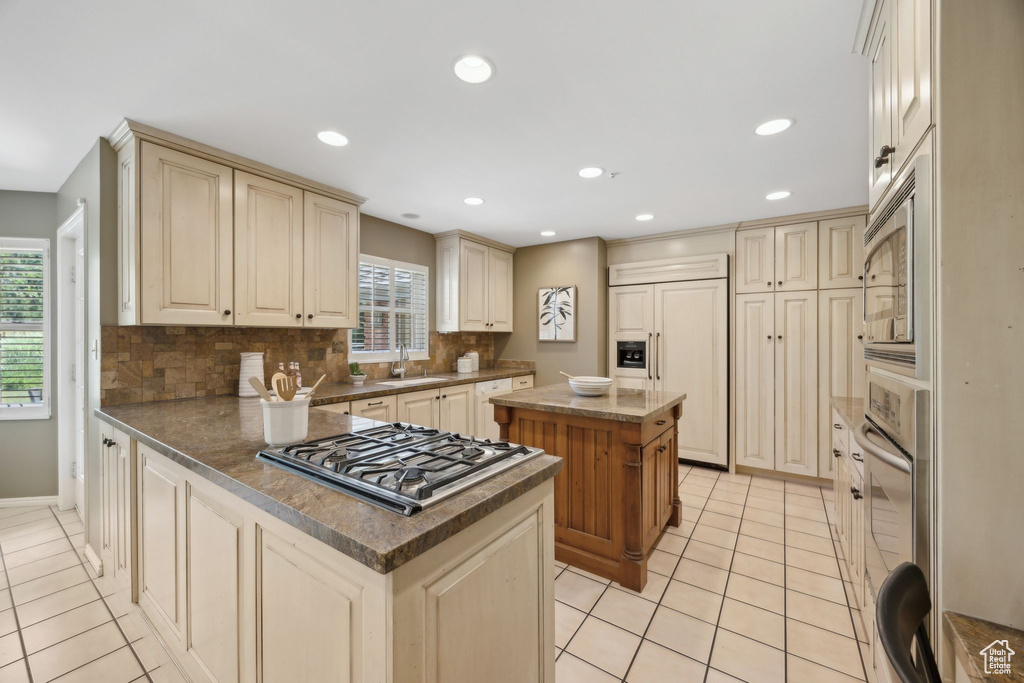 Kitchen featuring sink, light tile patterned floors, a center island, and decorative backsplash