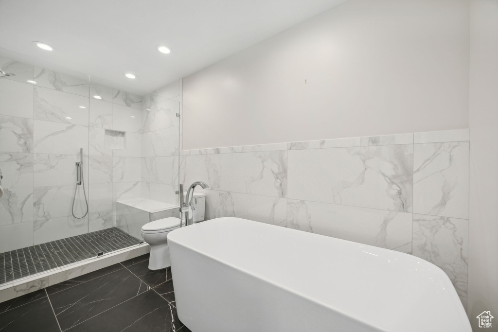 Bathroom with tile patterned flooring, tile walls, separate shower and tub, and toilet