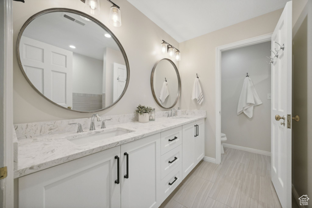 Bathroom featuring toilet, double sink vanity, and tile patterned flooring