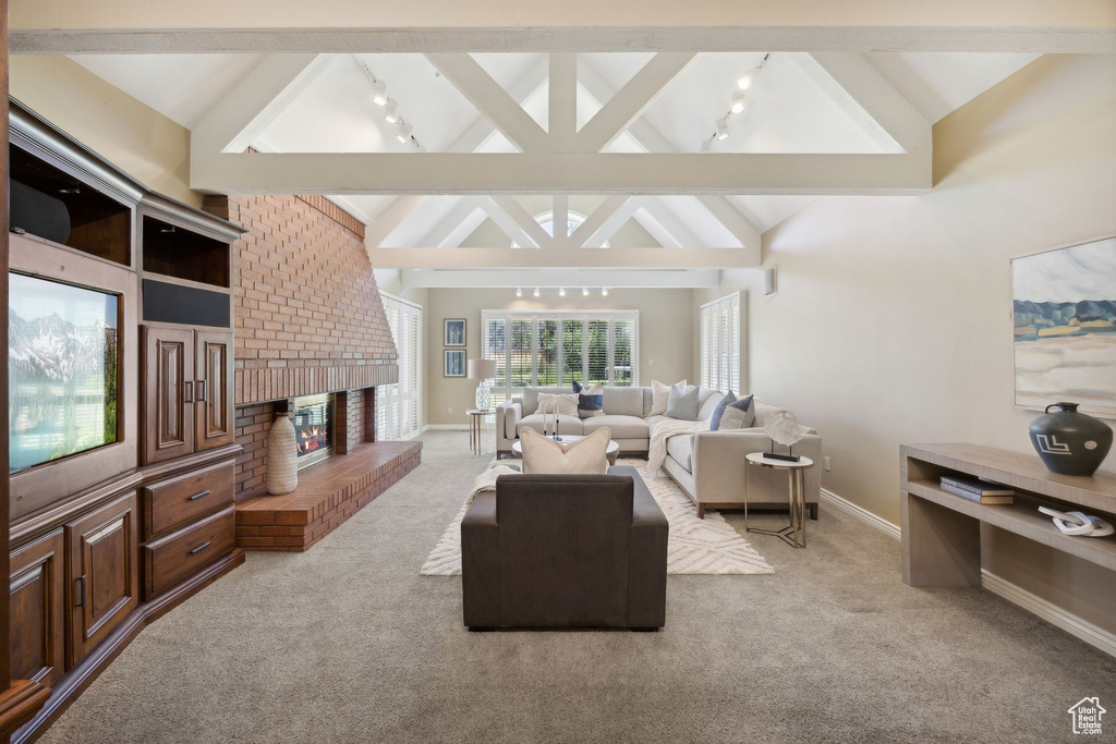 Living room with a fireplace, light colored carpet, beam ceiling, high vaulted ceiling, and brick wall