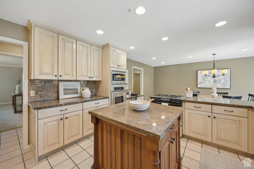 Kitchen featuring tasteful backsplash, hanging light fixtures, stainless steel microwave, light colored carpet, and a kitchen island