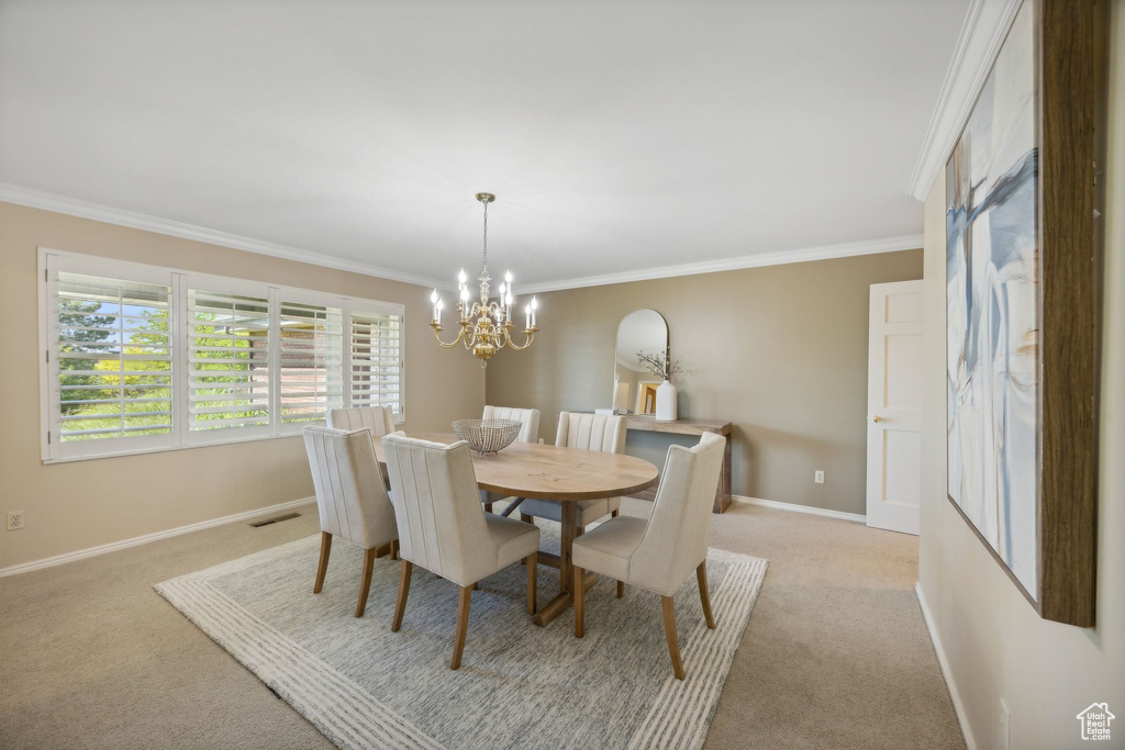 Carpeted dining space with crown molding and a chandelier