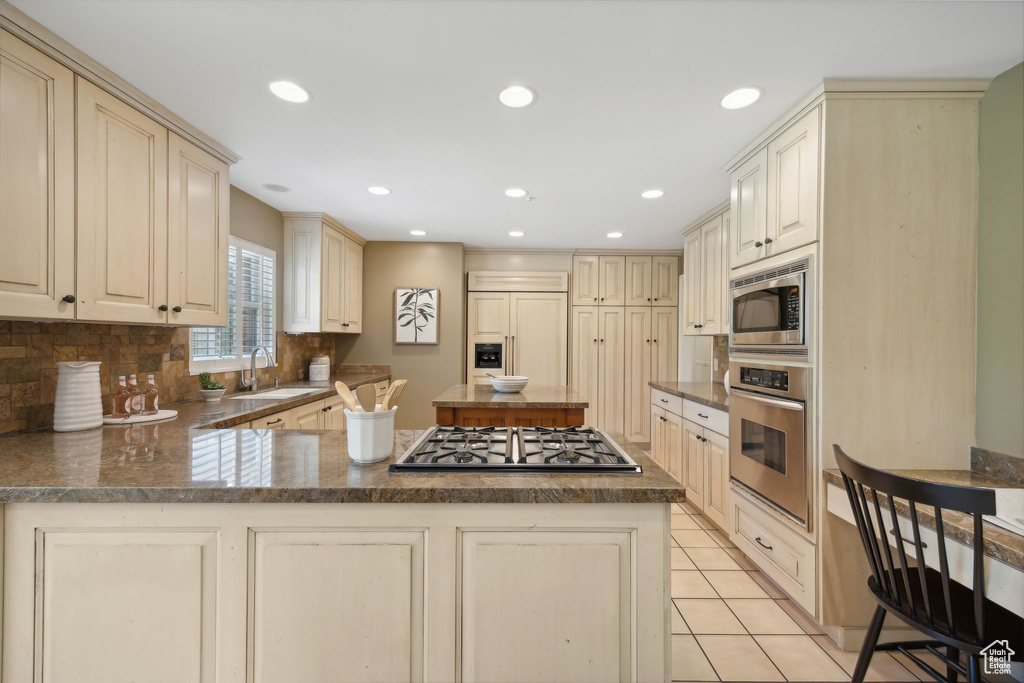 Kitchen with light tile patterned floors, backsplash, cream cabinetry, built in appliances, and sink