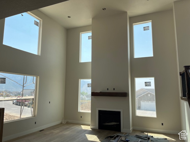 Unfurnished living room featuring light hardwood / wood-style floors, a high ceiling, and a healthy amount of sunlight