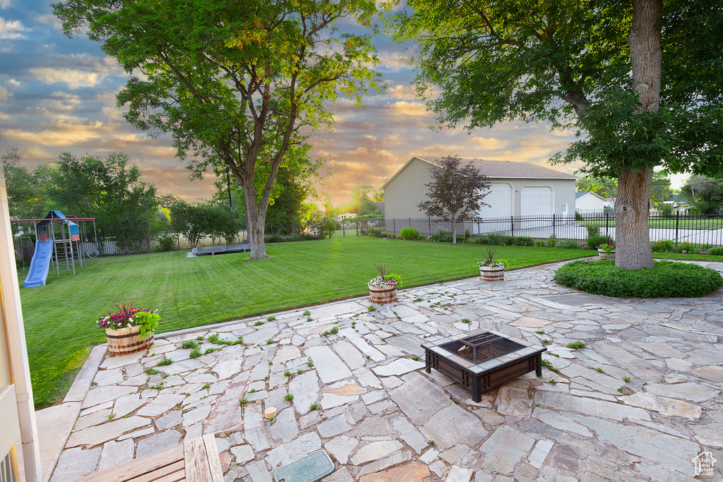 Patio terrace at dusk with a yard, a playground, and an outdoor fire pit