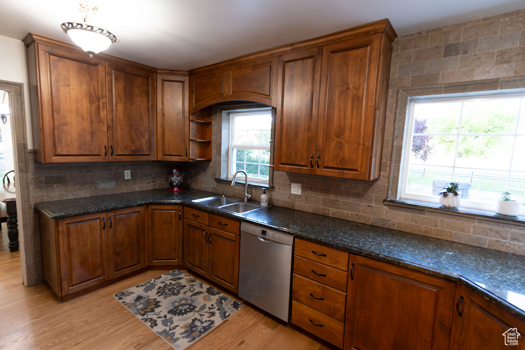 Kitchen with light hardwood / wood-style flooring, sink, backsplash, dark stone countertops, and dishwasher