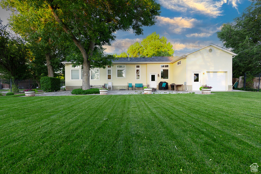 Back house at dusk with a garage, a patio area, and a lawn