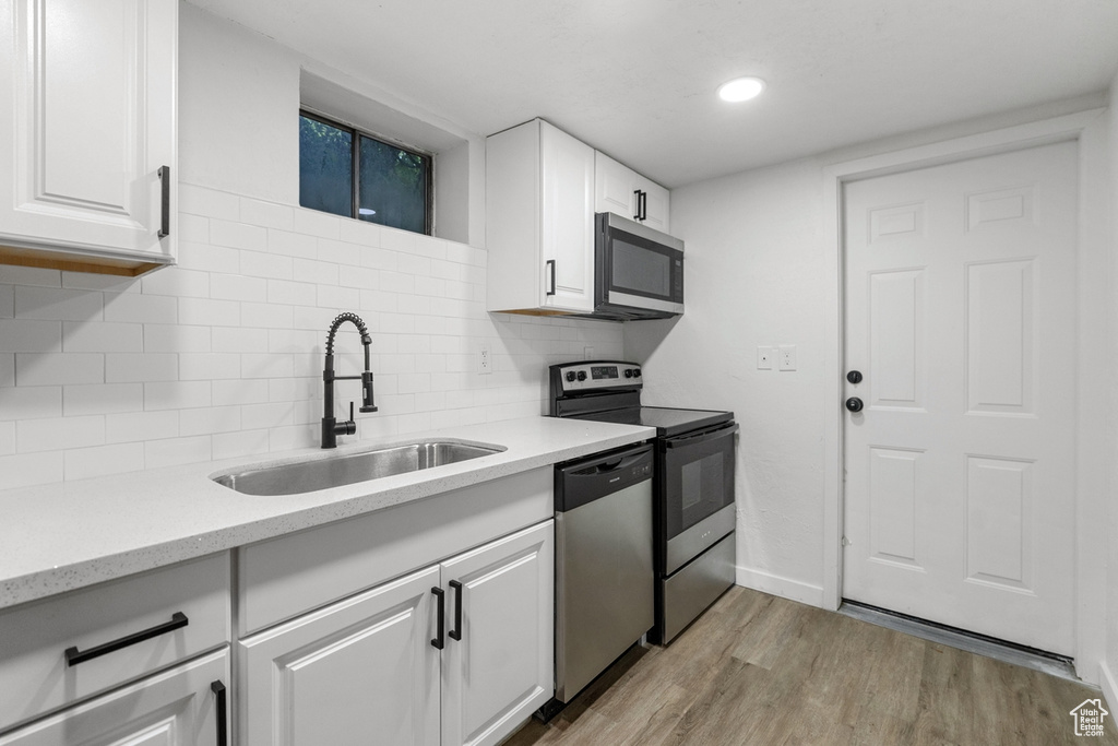 Kitchen featuring decorative backsplash, white cabinets, light wood-type flooring, sink, and appliances with stainless steel finishes